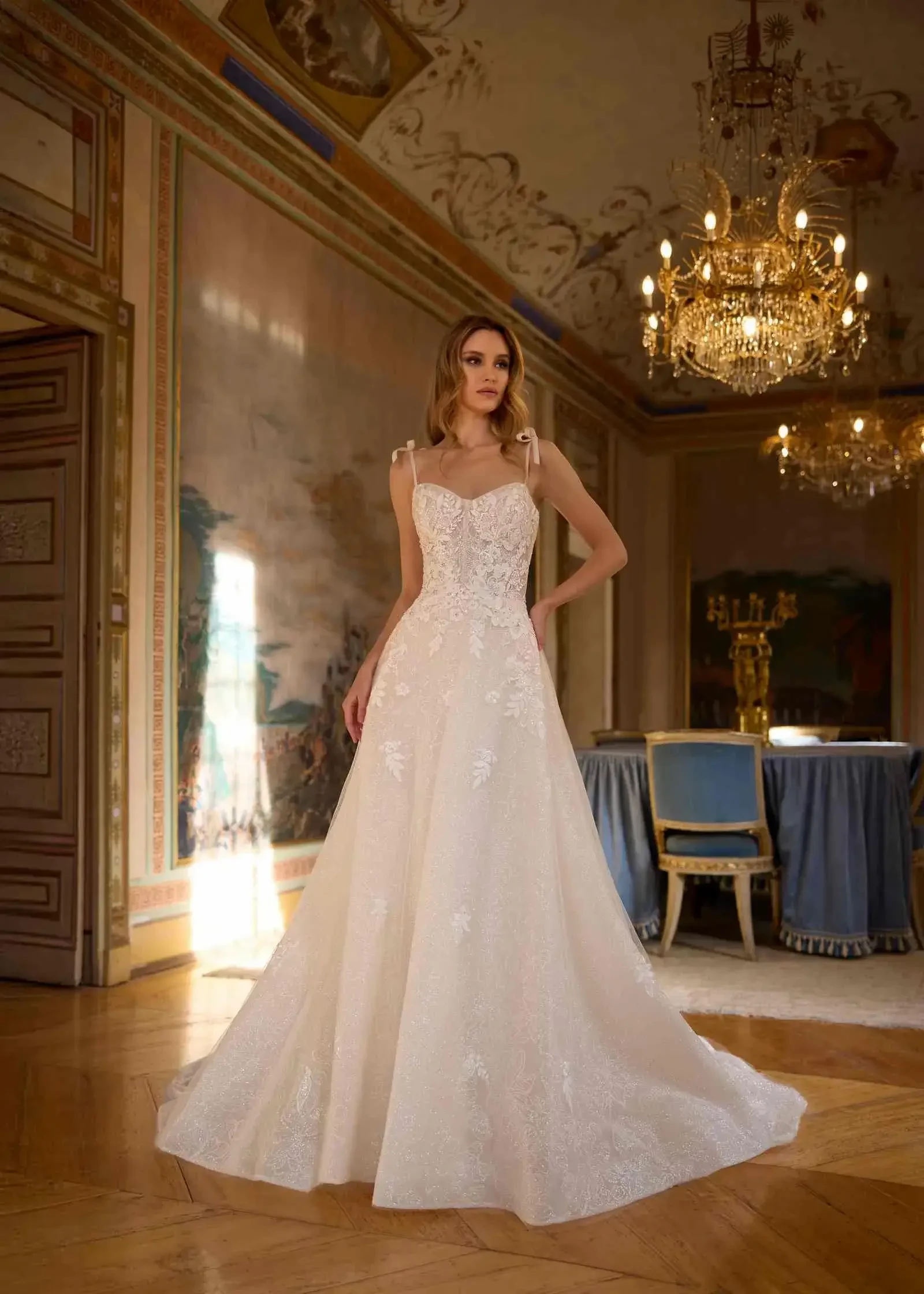 A woman in a wedding dress standing in an elegant room with chandeliers and classic decor.